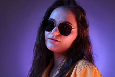 Portrait of beautiful young woman with stylish sunglasses on color background with neon lights