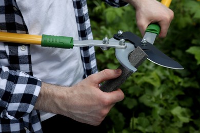 Photo of Man sharpening pruner outdoors, closeup. Gardening tools