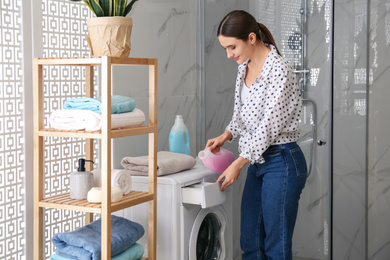 Photo of Woman pouring detergent into washing machine drawer in bathroom. Laundry day