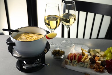 Photo of Fork with piece of apple, melted cheese in fondue pot, wine and products on grey table