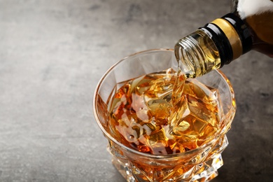 Pouring whiskey from bottle into glass with ice cubes on table. Space for text