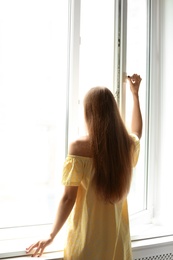 Young beautiful woman opening big window in room