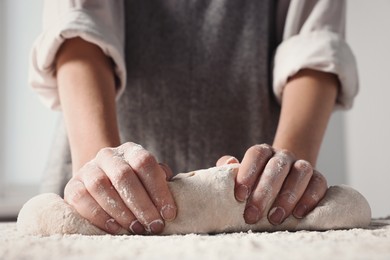Photo of Woman kneading dough at table in kitchen, closeup