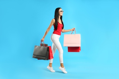 Photo of Beautiful young woman with paper shopping bags on light blue background