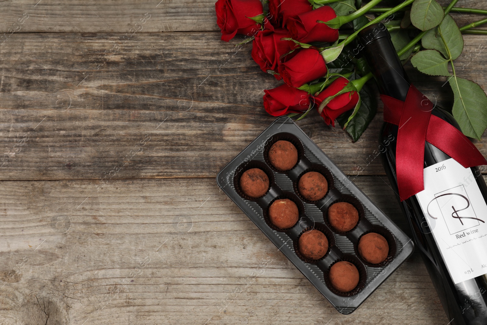 Photo of Bottle of red wine, chocolate truffles and roses on wooden table, flat lay. Space for text