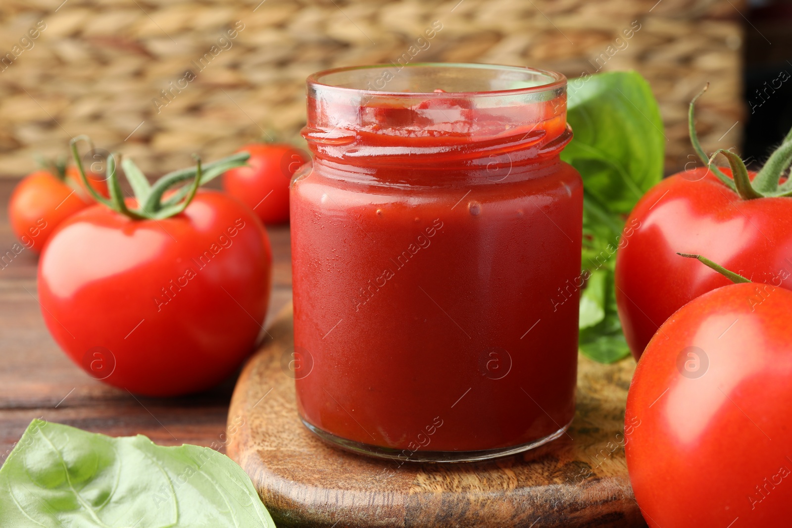 Photo of Jar of tasty ketchup and tomatoes on wooden table, closeup