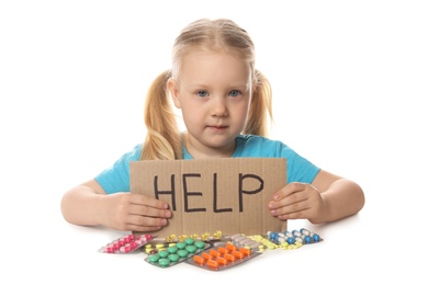 Photo of Little child with many different pills and word Help written on cardboard against white background. Danger of medicament intoxication