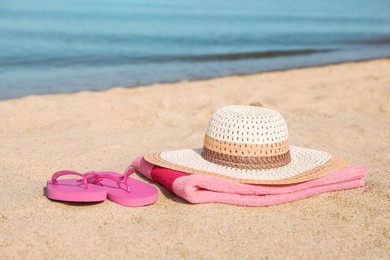 Beach towel with straw hat and slippers on sand near sea