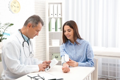 Doctor checking young woman's pulse with medical device in hospital