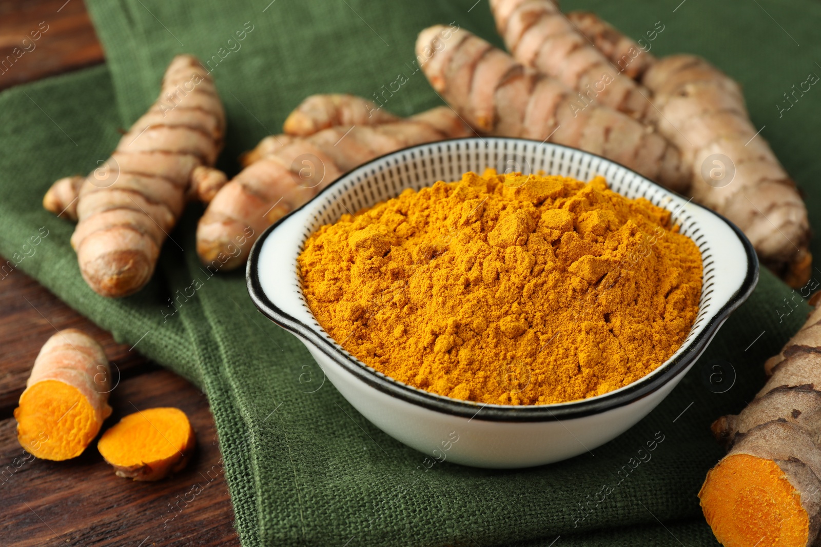 Photo of Bowl with aromatic turmeric powder and cut roots on wooden table, closeup