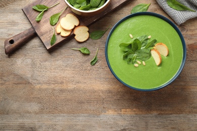 Flat lay composition with fresh green healthy spinach soup on wooden table, space for text