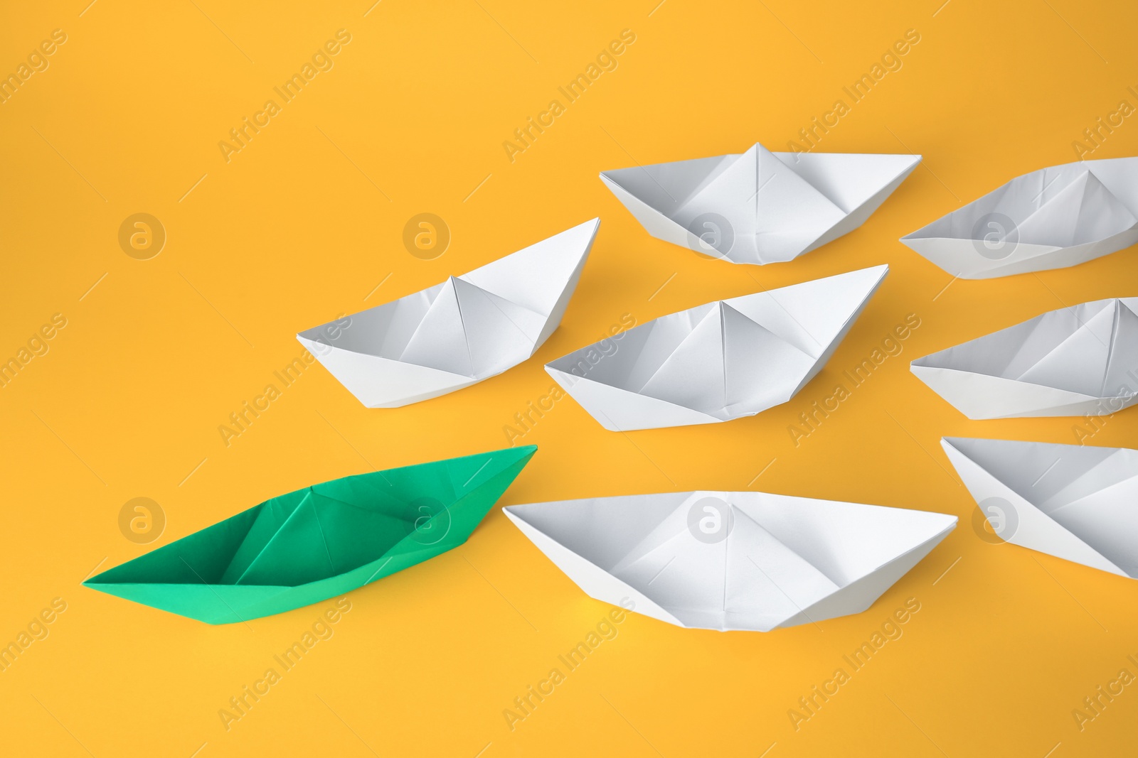 Photo of Group of paper boats following green one on yellow background. Leadership concept