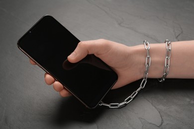 Photo of Internet addiction. Top view of man holding phone at wooden table, hand tied to device with chain