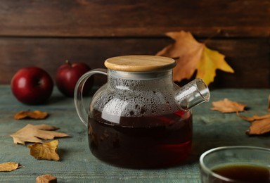 Photo of Glass teapot of hot beverage and autumn leaves on light blue wooden table