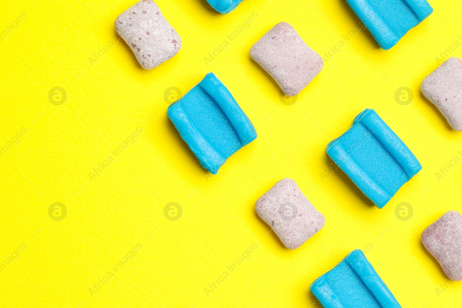 Photo of Different bubble gums on yellow background, flat lay. Space for text