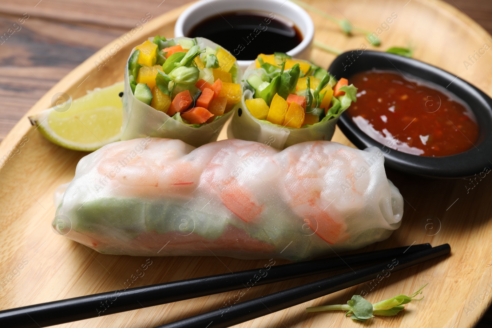 Photo of Tasty spring rolls and sauces on wooden plate, closeup