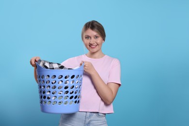 Photo of Happy woman with basket full of laundry on light blue background. Space for text
