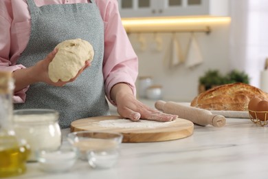 Photo of Making bread. Woman holding dough at white table in kitchen, closeup