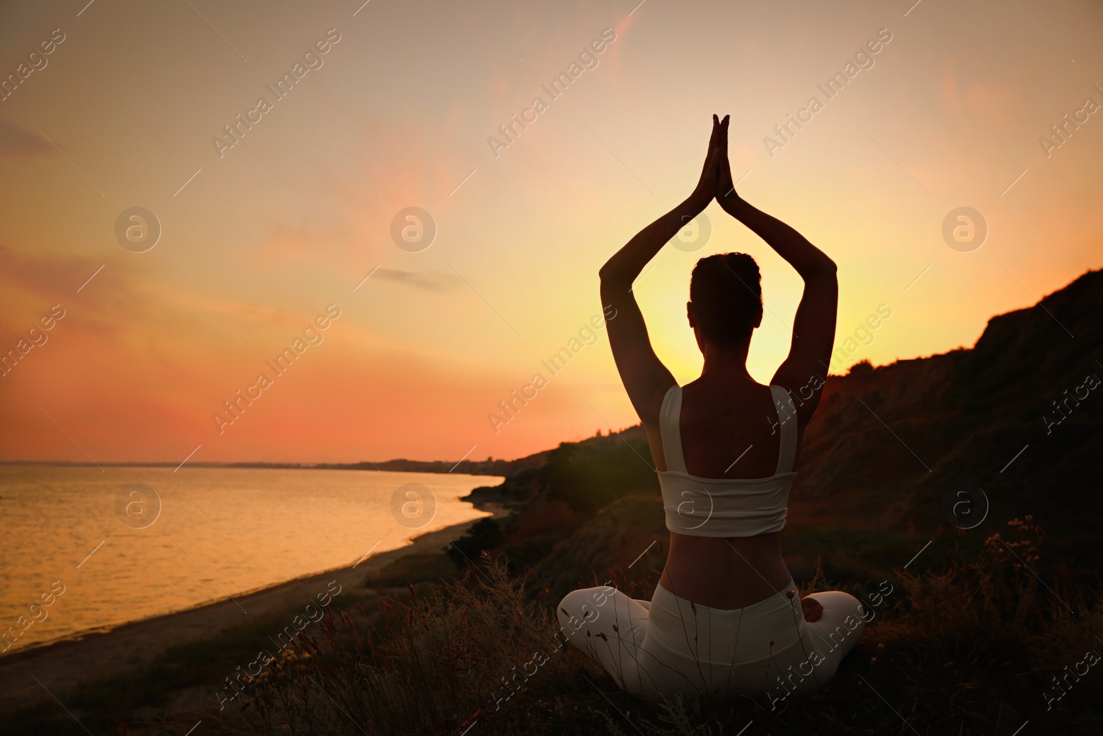 Photo of Woman meditating near sea at sunset, back view. Space for text