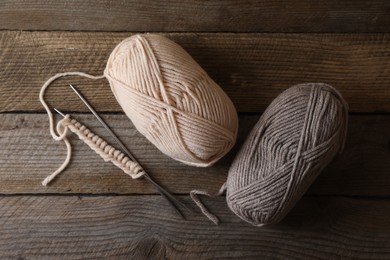 Soft colorful yarns, knitting and metal needles on wooden table, flat lay