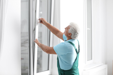 Photo of Mature construction worker repairing plastic window indoors