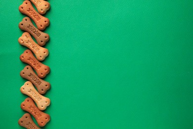 Photo of Bone shaped dog cookies on green background, flat lay. Space for text