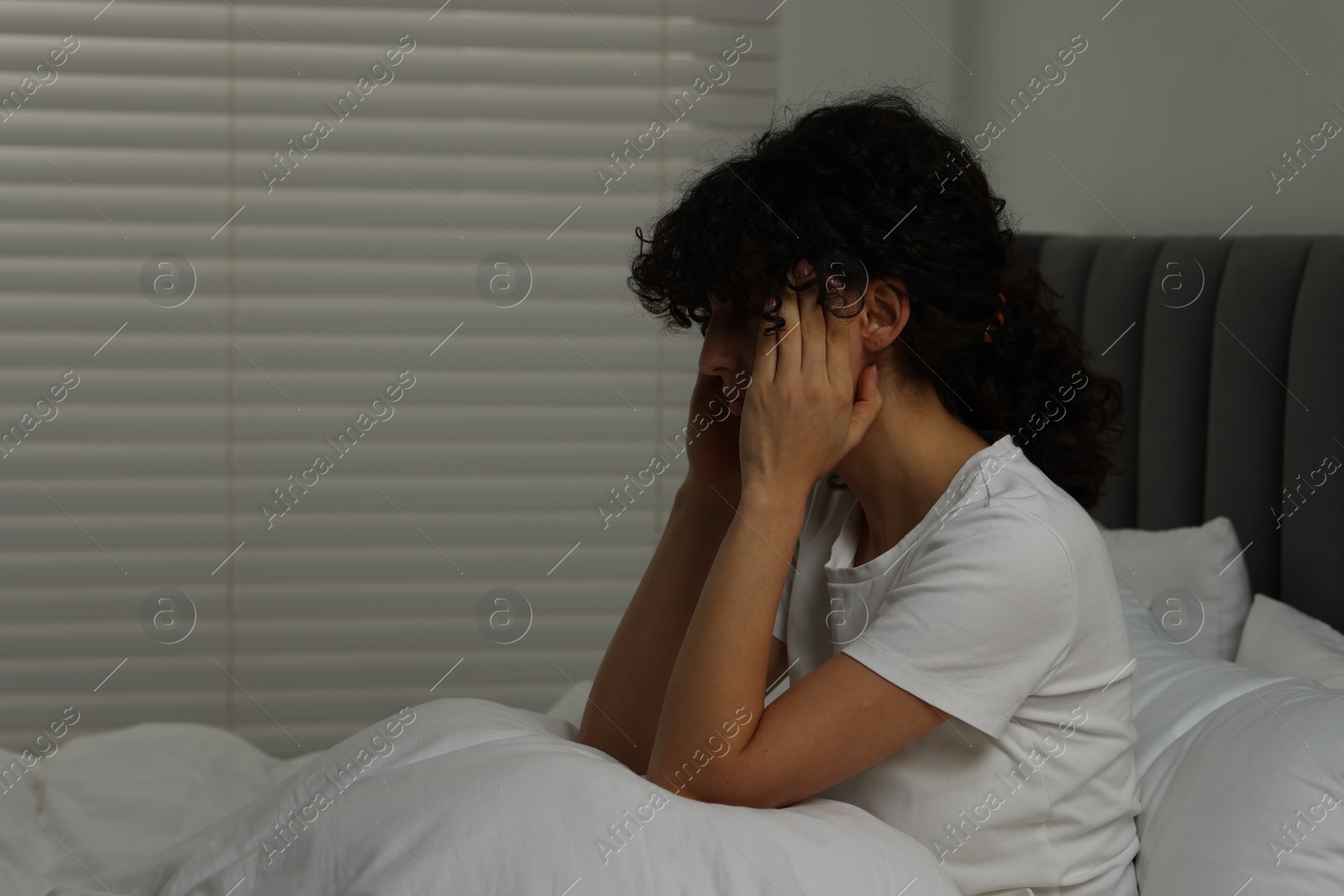 Photo of Young woman suffering from headache in bed at night