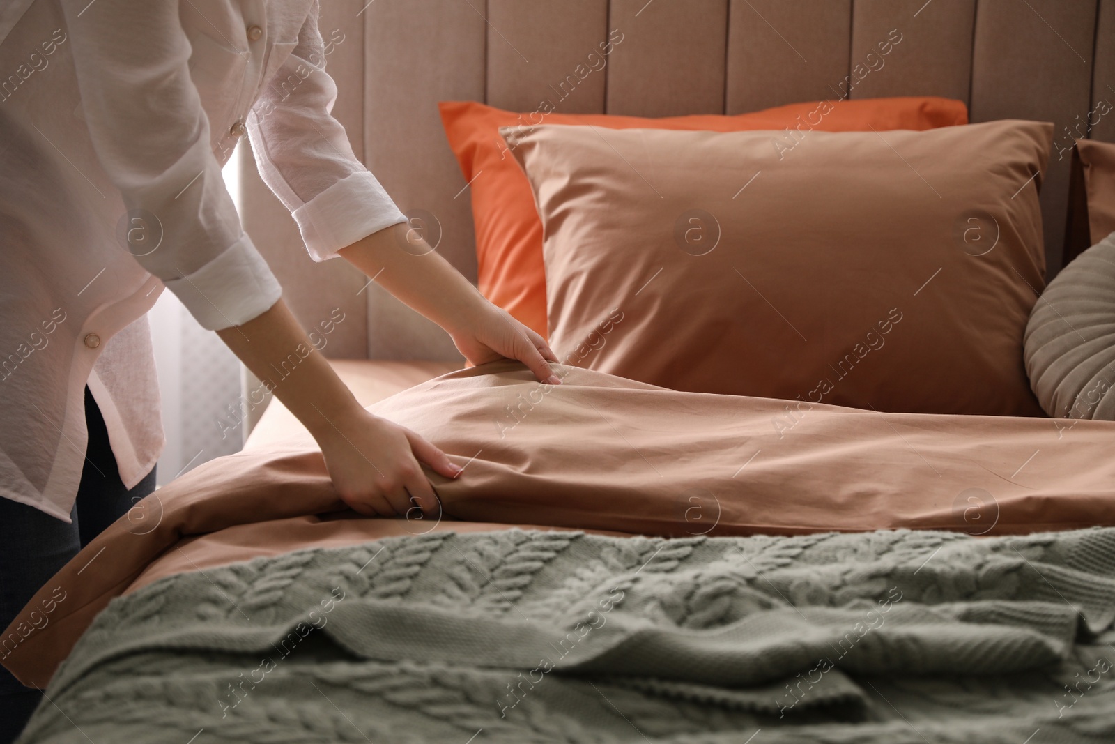 Photo of Woman making bed with stylish linens in room, closeup