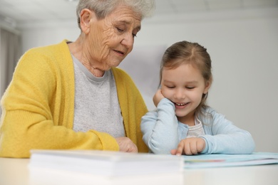 Photo of Cute girl and her grandmother reading book at home