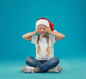 Photo of Cute little child wearing Santa hat on blue background. Christmas holiday