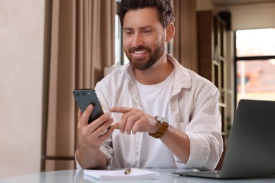 Photo of Handsome man sending message via smartphone at table indoors