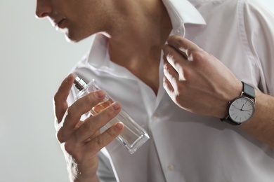 Handsome man applying perfume on neck against light background, closeup