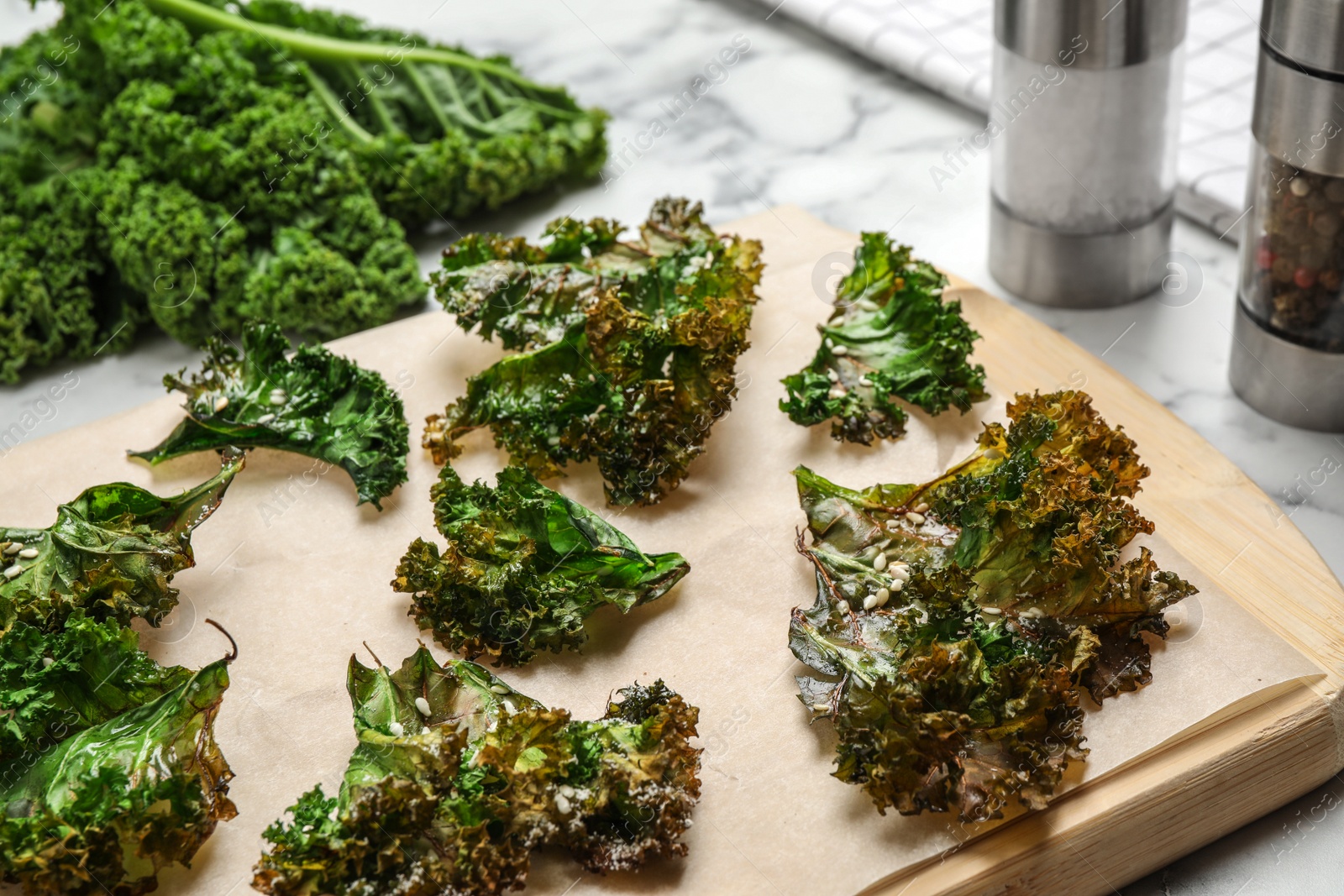 Photo of Tasty baked kale chips on wooden board