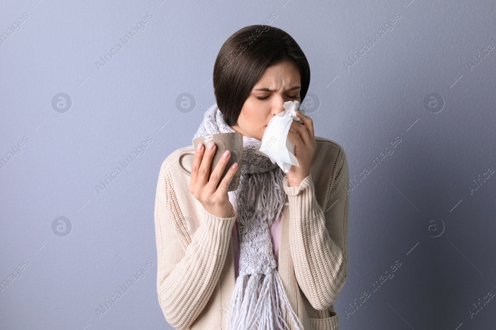 Photo of Young woman with cup of hot tea suffering from cold on color background