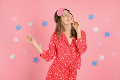 Beautiful woman wearing pajamas and sleep mask on pink background. Bedtime