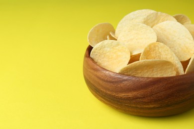 Bowl of tasty potato chips on yellow background, closeup. Space for text