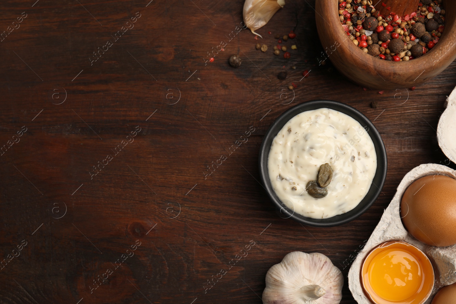 Photo of Creamy caper sauce in bowl and ingredients on wooden table, flat lay. Space for text