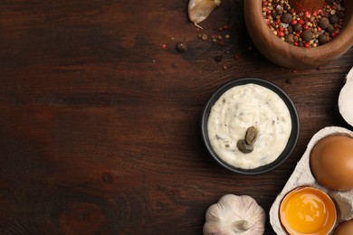 Photo of Creamy caper sauce in bowl and ingredients on wooden table, flat lay. Space for text