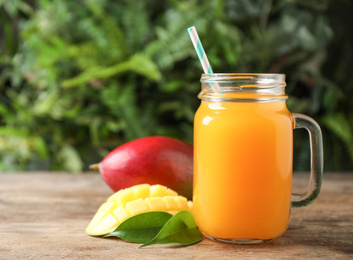 Mason jar of delicious mango drink on wooden table. Space for text