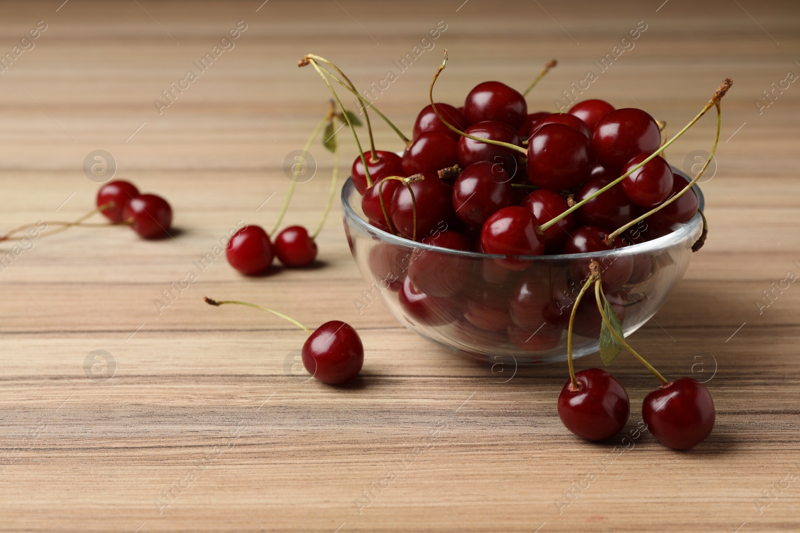 Photo of Glass bowl of delicious cherries on wooden table, space for text