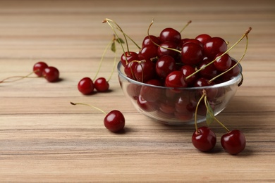 Photo of Glass bowl of delicious cherries on wooden table, space for text