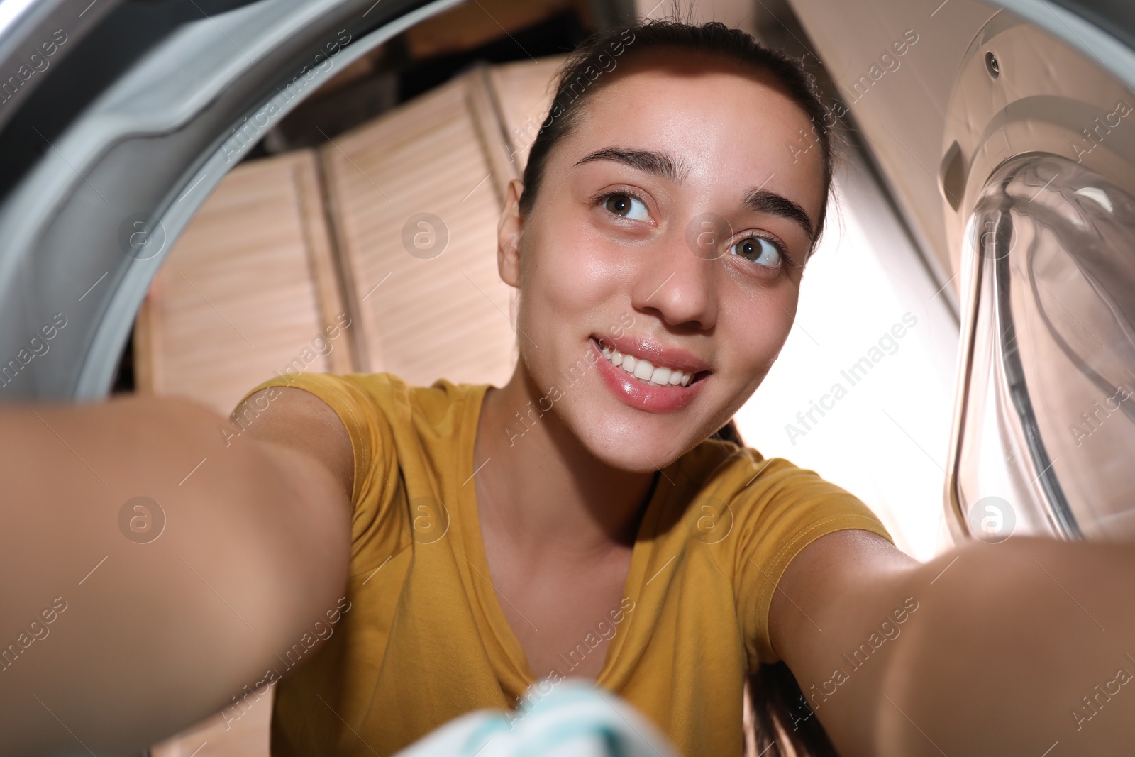 Photo of Woman putting clothes into washing machine in bathroom, view from inside. Laundry day