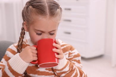 Cute girl drinking beverage from red ceramic mug at home, space for text