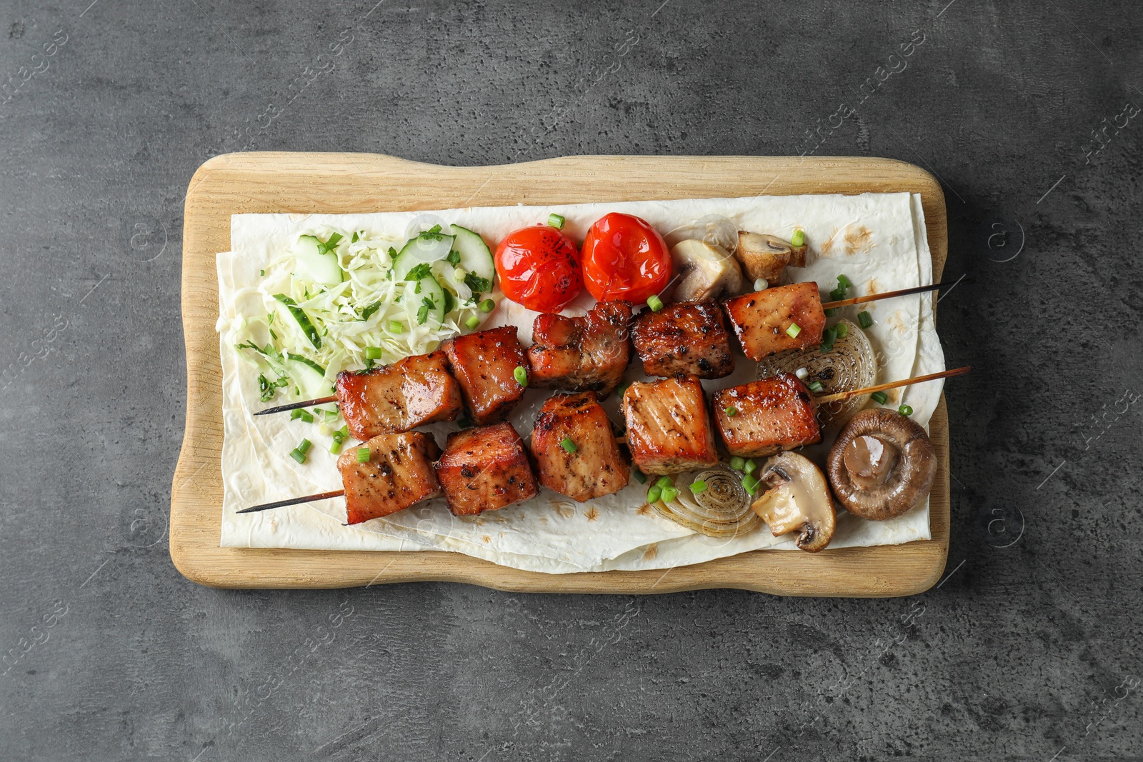 Photo of Delicious shish kebabs with vegetables and lavash on grey table, top view