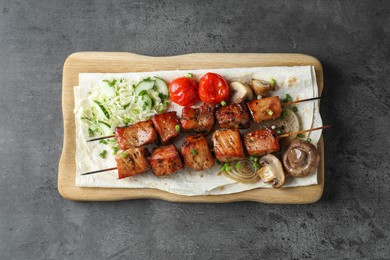 Photo of Delicious shish kebabs with vegetables and lavash on grey table, top view