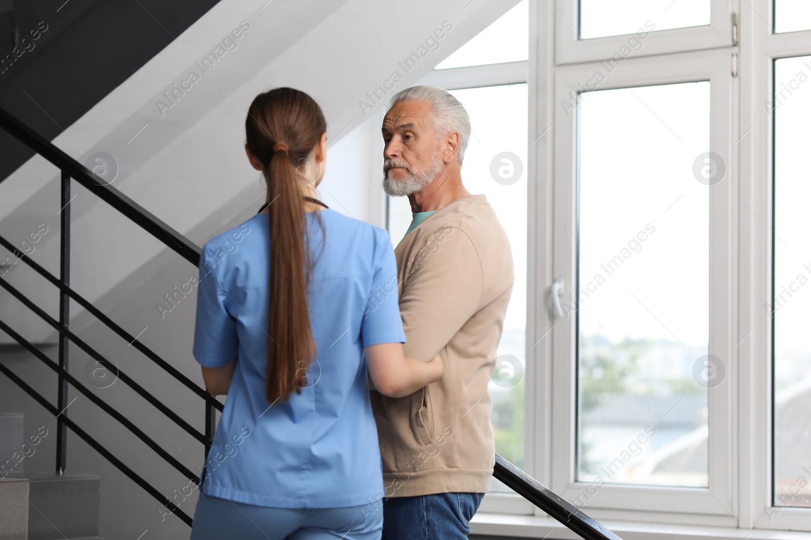 Photo of Young healthcare worker assisting senior man on stairs indoors