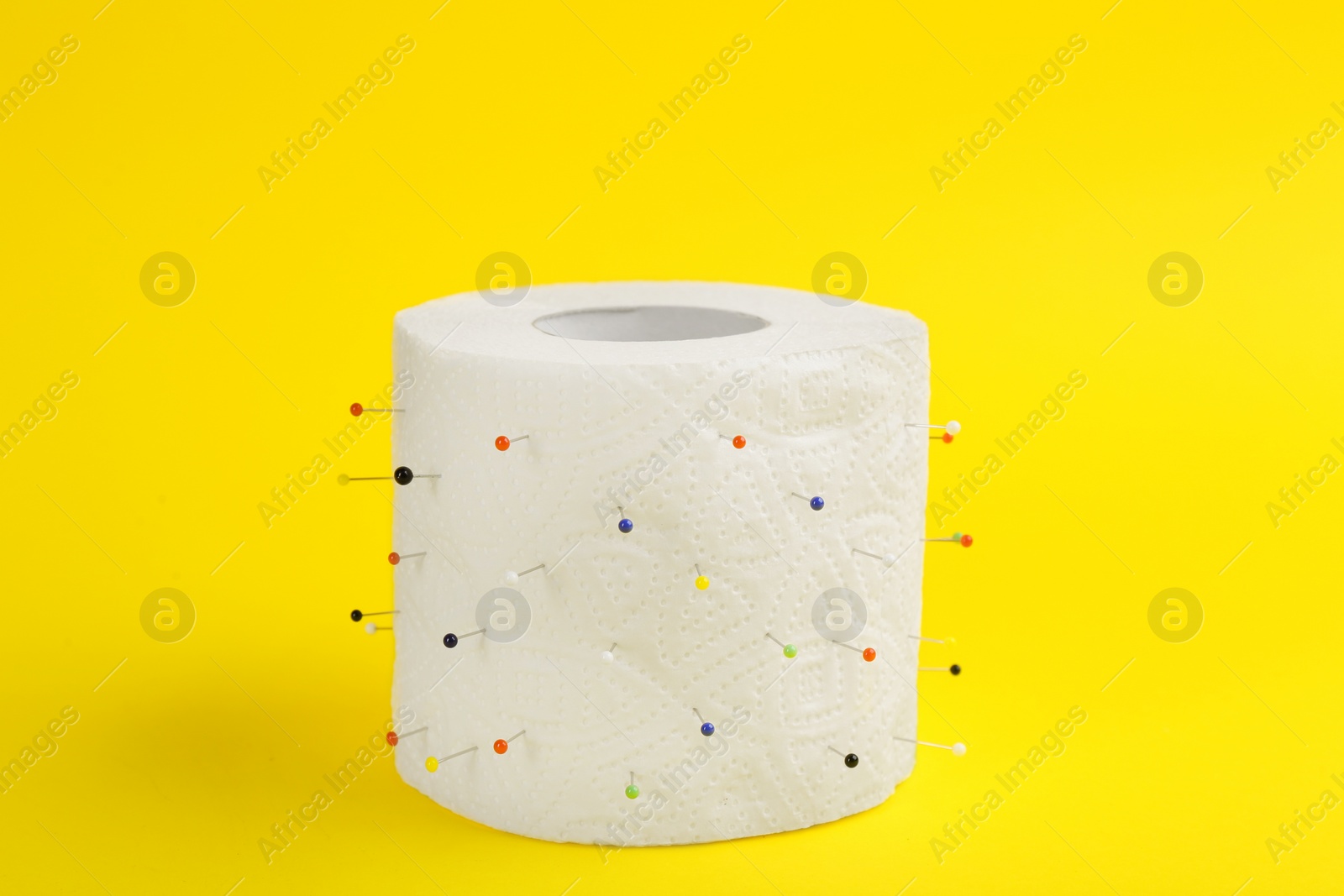 Photo of Roll of toilet paper with straight pins on yellow background. Hemorrhoid problems
