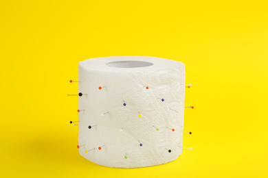 Photo of Roll of toilet paper with straight pins on yellow background. Hemorrhoid problems