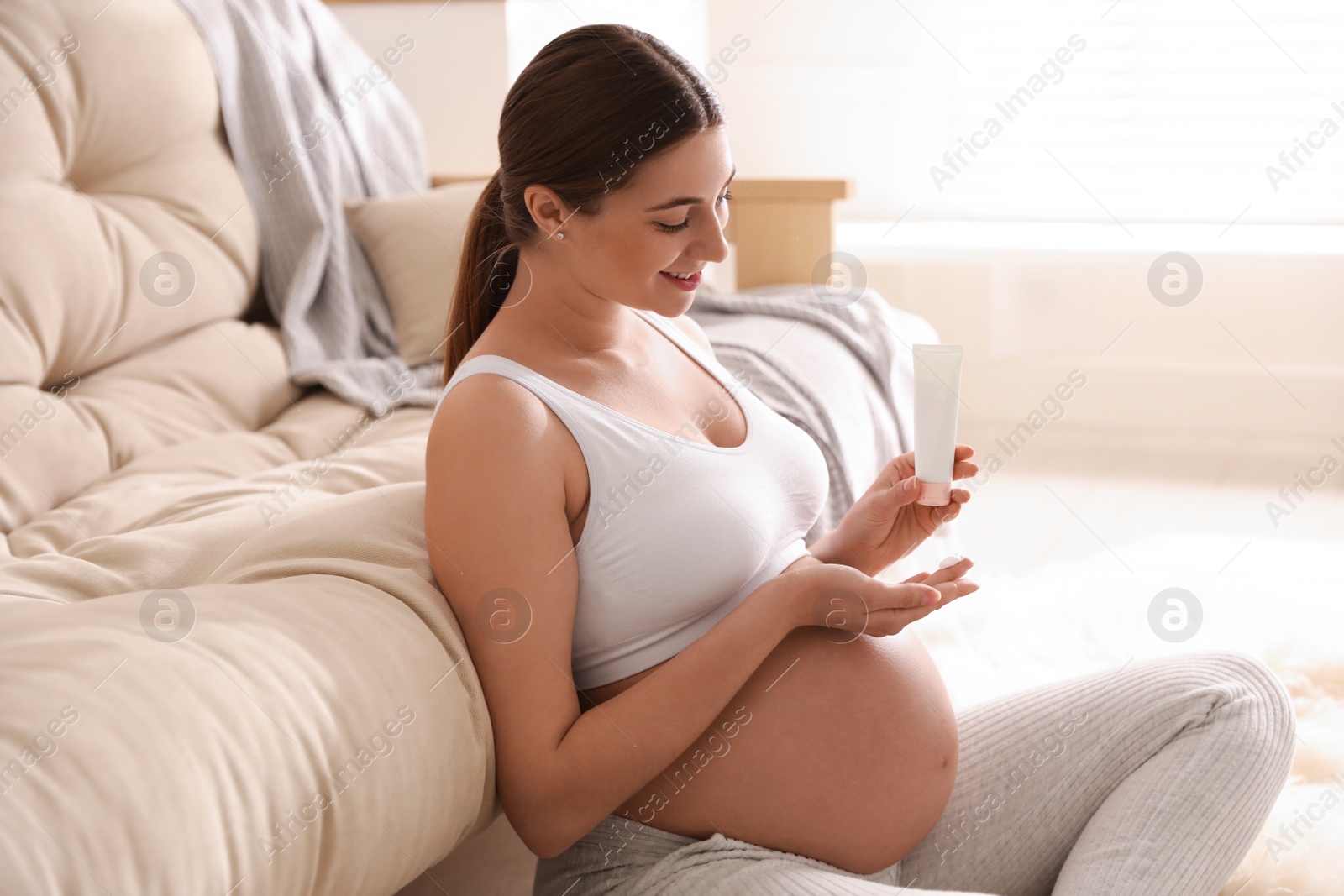 Photo of Young pregnant woman with cosmetic product at home