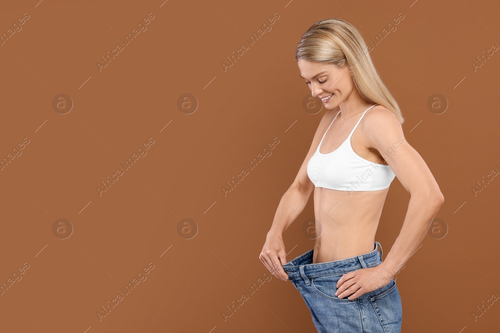 Photo of Slim woman wearing big jeans on brown background, space for text. Weight loss